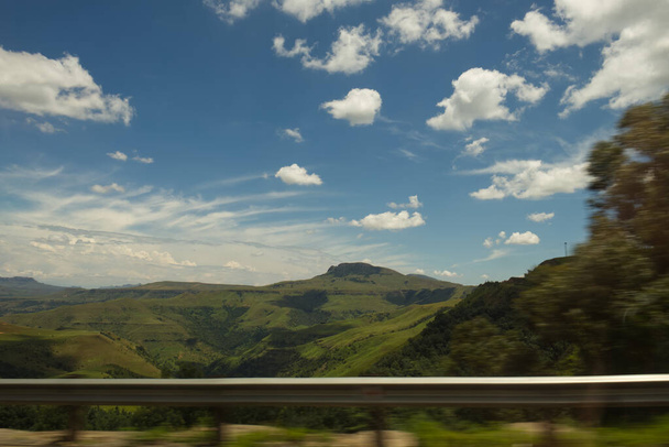 Yeşil dağların manzarası ve hareket halindeki arabadan alınan vadi mavi gökyüzü ve kabarık beyaz bulutlarla. - Fotoğraf, Görsel