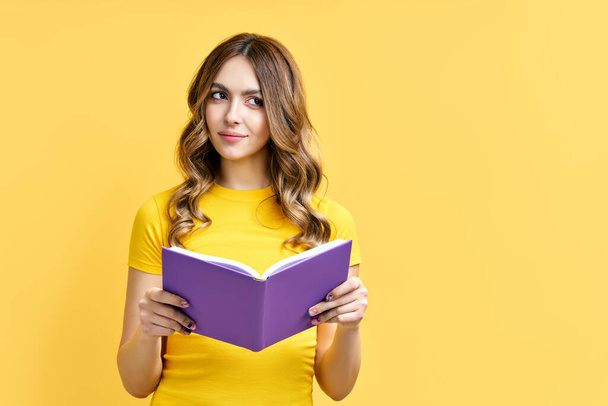 Dreamy positive girl rest with book on yellow background with copy space - Valokuva, kuva