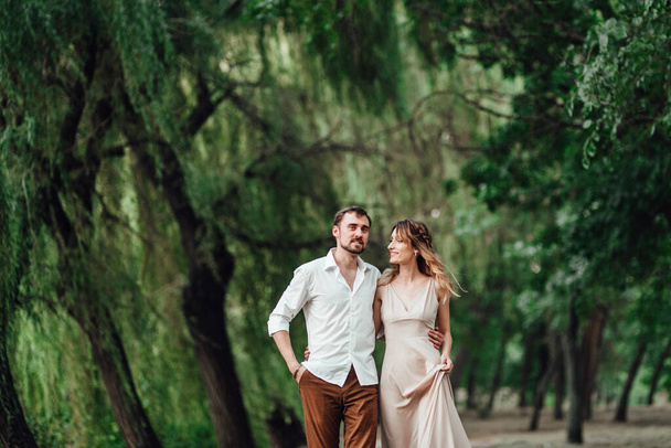 a guy and a girl are walking along the banks of a wild river overgrown with willows and forest - Foto, imagen