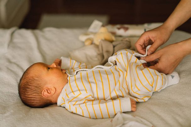Anya cuki újszülött kisfiút öltöztet kezeslábasba.. - Fotó, kép