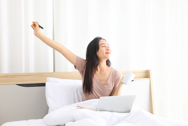 Asian woman stretching after working from home using laptop computer while drinking coffee with copy space - Foto, Bild