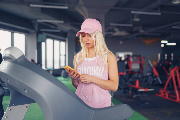 Side view of sporty blonde woman exercising on treadmill in gym - Foto, Imagen