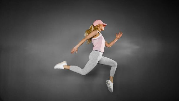 Young woman with fit body jumping and running against grey backg - Foto, Imagem