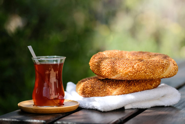 Geleneksel Türk simitli simit ve ahşap zemin üzerinde sert güneş ışığı gölgeli Türk çayı. Sokak yemeği. Lezzetli bir kahvaltı. Doğa arkaplanı  - Fotoğraf, Görsel