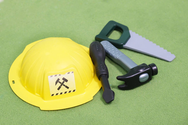 Kids builder toy set. Plastic yellow construction hard hat and tool kit hammer, saw and screwdriver. Playing in the profession, role-playing games in kindergarten - Fotó, kép