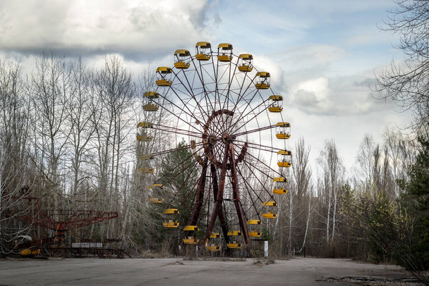 Old abandoned rusty metal radioactive yellow ferris wheel against dramatic sky in amusement park in ghost town Pripyat, Chernobyl Exclusion Zone - Φωτογραφία, εικόνα