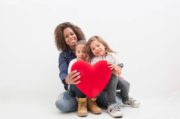 Happy Brazilian mother with two children, with red heart in their hands, on the white background. Multiethnic children. Happy mother's day concept - Photo, Image