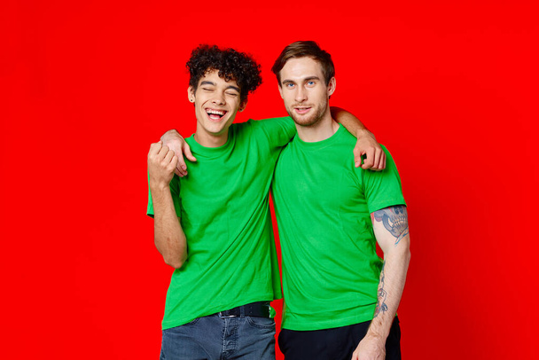 Two man green t-shirts embrace emotions friendship red background - Foto, Imagen
