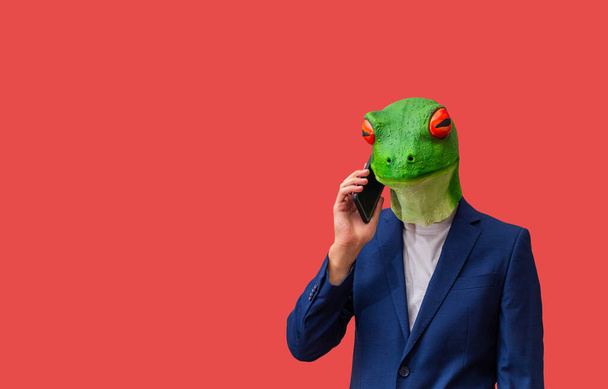 man with googly-eyed frog mask calling with smart phone on red background with copy space - Photo, Image