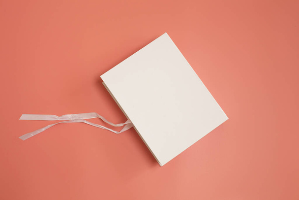 Белая подарочная коробка с развязанным шелковым бантом на розовом фоне - Фото, изображение