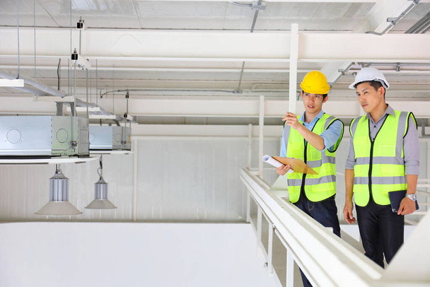 Два азиатских инженера-подрядчика в технике безопасности во время осмотра и обсуждения будущего расширения бизнес-плана завода внутри склада - Фото, изображение