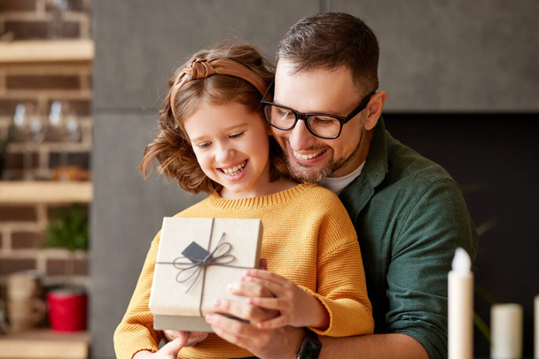 Portrait of young loving father wearing eyeglasses giving his happy cute daughter birthday or christmas present, wrapped gift box with bow, selective focus. Family holidays and celebration concept - Фото, изображение