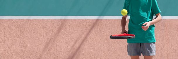 Concept de sport de tennis pour enfants. Joueur de tennis enfant garçon jouant et s'entraînant avec raquette et balle sur fond de mur de tennis bleu et orange. Large bannière avec espace de copie - Photo, image