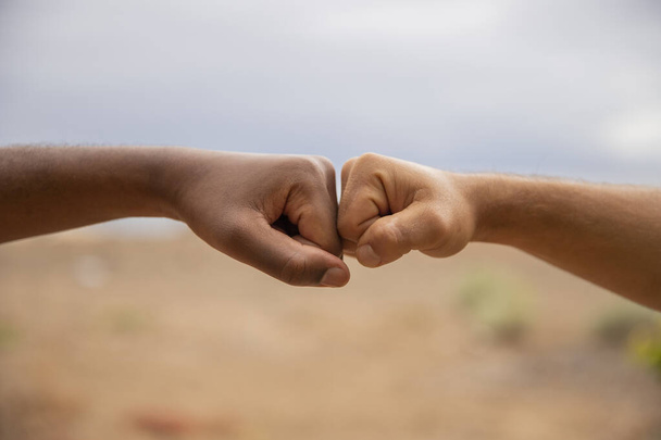 Handen van verschillende kleur om racisme te bestrijden. Twee vuisten raken, een is wit (Kaukasisch) de andere is zwart (Afrikaans))  - Foto, afbeelding