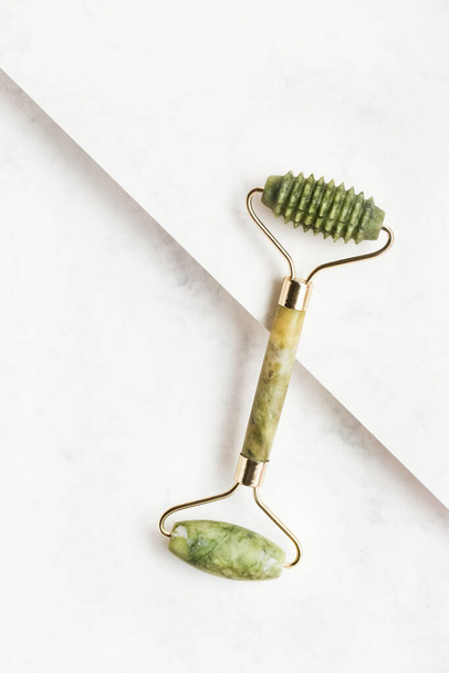 Green face roller from natural jade stone on a white background. Top view, copy space for text - Photo, Image