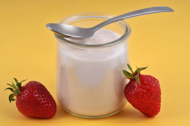 yogurt alla fragola con un cucchiaio primo piano su sfondo giallo - Foto, immagini