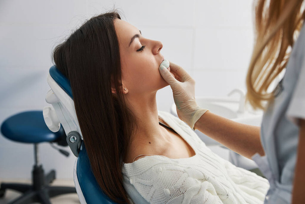 Dental office employee taking out teeth impression from lady mouth - Φωτογραφία, εικόνα