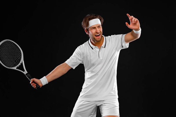 Tennis player with racket in white costume. Man athlete playing isolated on black background. - Foto, afbeelding