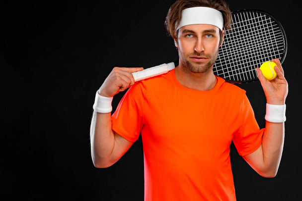 Tennis player with racket in orange t-shirt. Man athlete playing isolated on black background. - Fotoğraf, Görsel