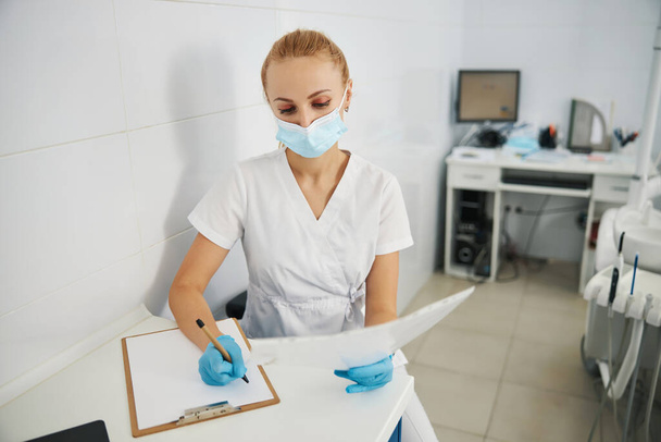 Woman dental practitioner copying results of x-ray to paper - Φωτογραφία, εικόνα