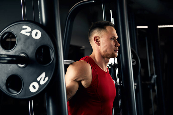 Retrato de cerca de un entrenamiento de hombre musculoso con barra de pesas en el gimnasio. Brutal culturista atlético hombre con seis pack, abdominales perfectos, hombros, bíceps, tríceps y pecho - Foto, Imagen