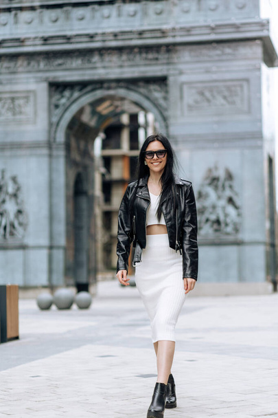 Young beautiful brunette in sunglasses and a fashionable outfit walking in the city - Foto, afbeelding