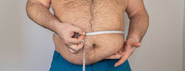 De dikke man meet de grootte van de buik met een centimeter meetlint. persoon is overgewicht, hij is zwaarlijvig. beginnen met een dieet - Foto, afbeelding