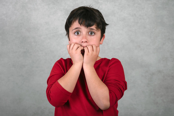 Gruseliges Kind, das seine Fingernägel auf grauem Hintergrund beißt - Foto, Bild
