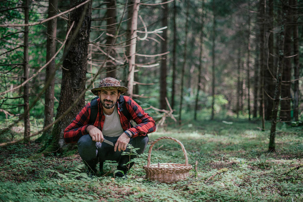 Ein junger männlicher Pilzsammler mit einem großen Korb sucht, sammelt Pilze im Wald. Pilze sammeln in der Saison. - Foto, Bild