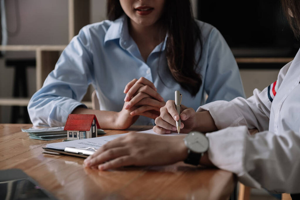 Image of real estate agent assisting client to sign contract paper at desk with house model - 写真・画像