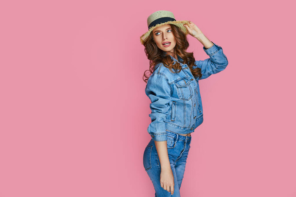Modern attractive young woman in blue stylish denim jacket in fashionable jeans stands near pink wall in the studio. Beautiful trendy girl fashion model posing indoors. Casual style.  - Foto, Imagem