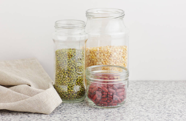 Variety of dry legumes: kidney bean, peas, green gram in glass jars uncooked on white kitchen background, zero waste, eco friendly, balanced diet food, healthy clean eating, vegan protein concept - Фото, изображение
