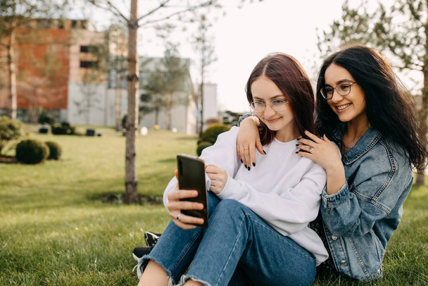 公園の二人の姉妹、笑顔とスマートフォンで自分の肖像画を撮る. - 写真・画像