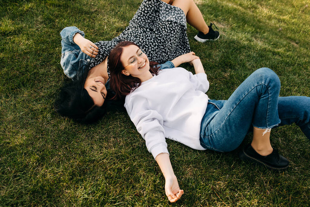 Two best friends spending time outdoors, lying on green grass in a park, laughing. - Photo, Image