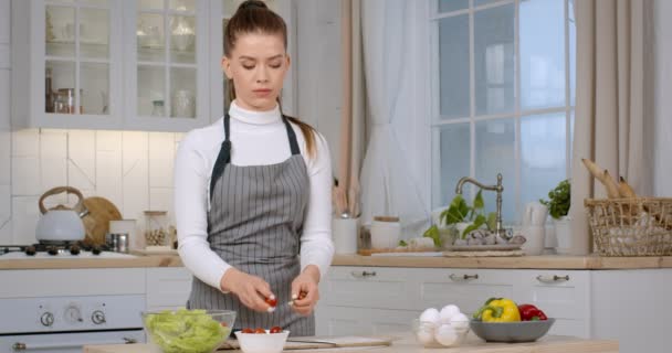 Giovane casalinga che cucina in cucina, tagliando pomodori biologici freschi per insalata di verdure, preparando la cena a casa - Filmati, video