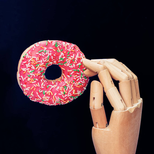 Bright glazed donut and wooden hand on dark background close-up. Concept of catering, consumerism, food, lifestyle - Fotoğraf, Görsel