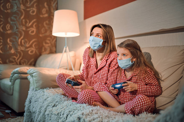 Woman and young girl wearing pajamas and medical protective mask - Foto, Imagen