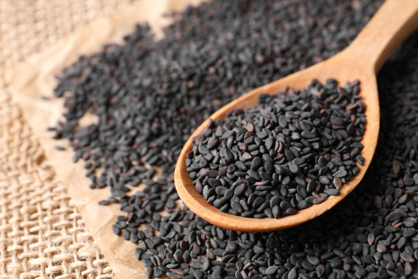 Black sesame seeds and wooden spoon on sack mat, closeup - Фото, изображение