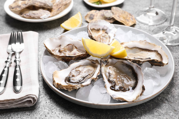Fresh oysters with lemon and ice on grey table, closeup - Foto, Imagem