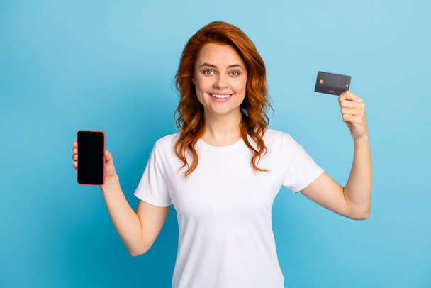 Photo portrait of woman holding mobile phone with blank space credit card in hands isolated on pastel blue colored background - Foto, afbeelding