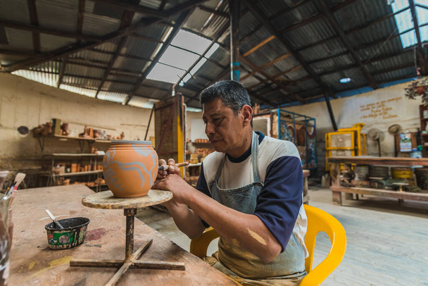 Μεξικανός τεχνίτης αγγειοπλαστών, που εργάζεται τον πηλό με τα χέρια του στο εργαστήριό του για τη δημιουργία γλυπτών, αγγείων, κανών, αγγείων κ.λπ., με παραδοσιακές μεθόδους. - Φωτογραφία, εικόνα