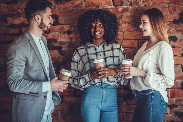 Group of young stylish happy people leaning against the wall and talking while drinks coffee in the paper cup. - Photo, image