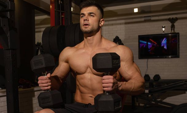 muscular shirtless young athlete training with dumbbells in gym - Φωτογραφία, εικόνα