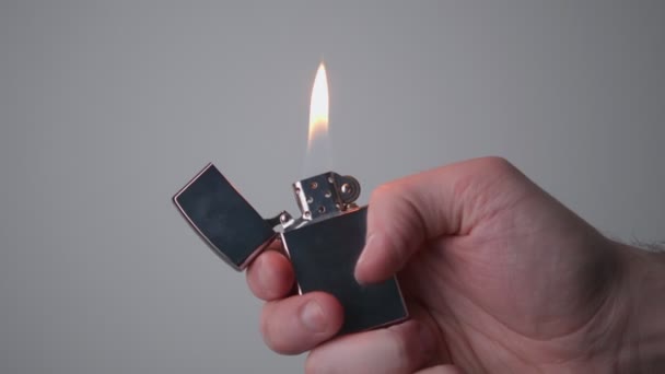 De man opent een metalen benzine aansteker, slaat op silicium en ontsteekt een vlam, de aansteker brandt, waarna hij blust de aansteker door het sluiten van het deksel, het concept van het afzuigen van vuur. - Video