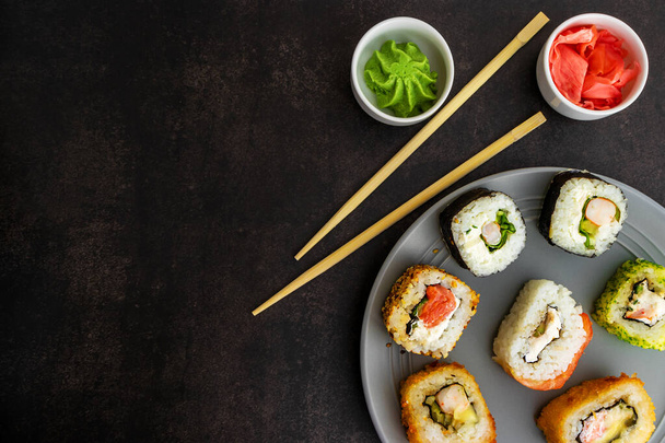 Sushi de diferentes opciones en una placa gris sobre un fondo cerrado, vista superior, con wasabi y jengibre - Foto, Imagen
