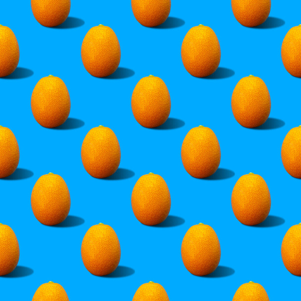 Colorato ed estivo modello di sfondo ora illustrazione di kumquat freschi gialli che gettano ombra dura sulla superficie blu vivida. Concetto di cibo estivo minimo - Foto, immagini
