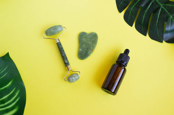 Jade gua sha scraper, roller facial massager and cosmetic oil with monstera leaf. The concept of self-care. Facial care. Zero waste. Lifting and toning treatment at home. - Photo, Image