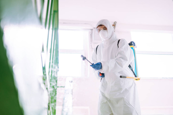 Hombre con traje protector desinfectando la entrada de un edificio residencial con aerosoles químicos para prevenir la propagación del coronavirus, pandemia en la ciudad de cuarentena. Covid -19. Concepto de limpieza. - Foto, imagen