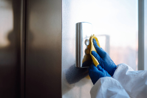 Cleaning and disinfection of the elevator to prevent COVID-19. Worker wearing protective suit sprays disinfectant buttons of the lift.  - Фото, зображення