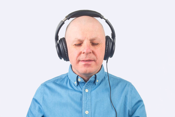 portret mężczyzny w niebieskiej koszuli ze słuchawkami w relaksie słuchającego muzyki na jasnym tle - Zdjęcie, obraz